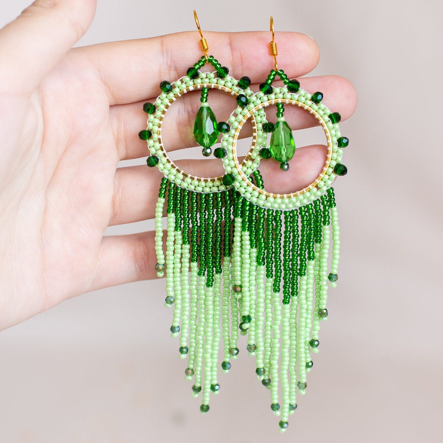 a pair of green beaded earrings hanging from a tree branch